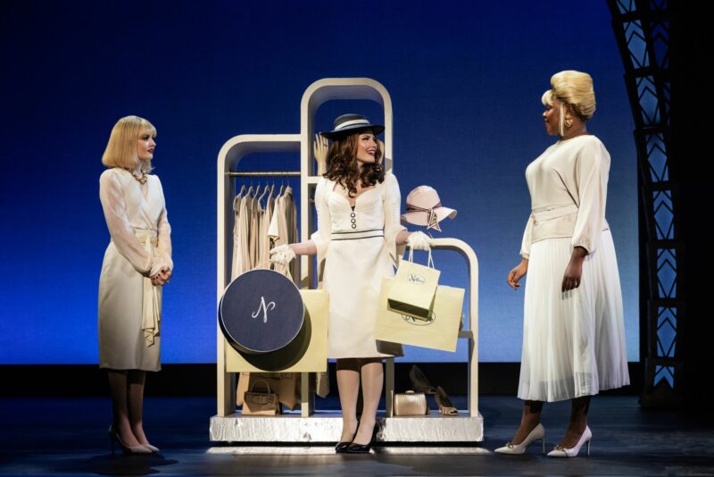 Bethany McDonald, Ellie Baker and Taylor M. Sheppard in Pretty Woman the Musical. Vivian stands between two shopkeepers holding multiple shopping bags.